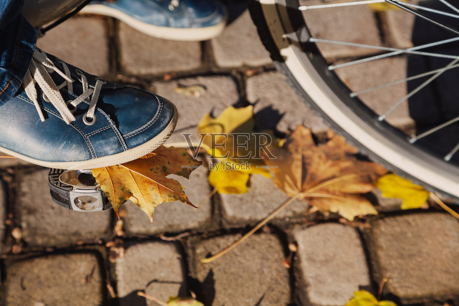 穿着运动鞋蹬着自行车在秋天的人行道上行走照片摄影图片