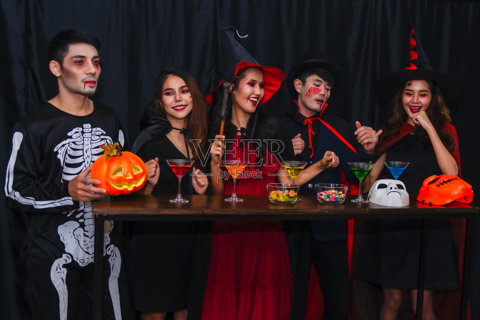 一群快乐的亚洲年轻人穿着cosplay和化妆一起在万圣节和站在聚会乐趣和喝鸡尾酒在夜总会。照片摄影图片