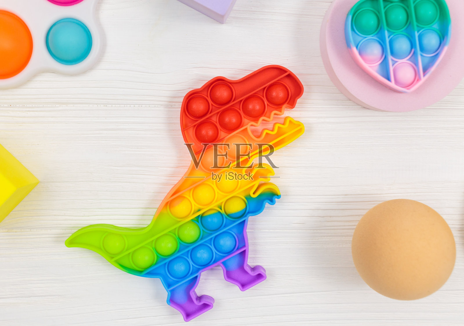 流行的硅胶恐龙抗压力流行玩具上的白色木制背景。时尚的缓解压力感官烦躁玩具。有趣的泡泡多色小玩意为成人和儿童照片摄影图片