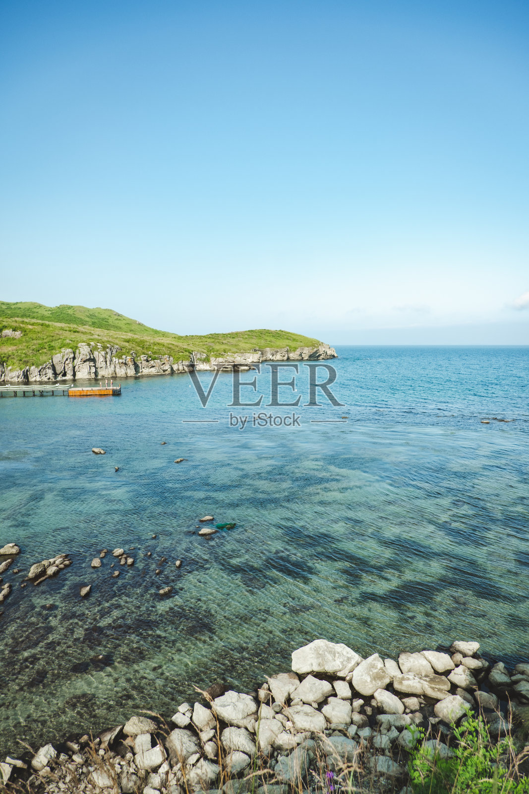 夏天海洋全景。一个浅浅的,清澈的,透明的海洋,周围有礁石,岩石和绿色的山丘。日本海洋。照片摄影图片