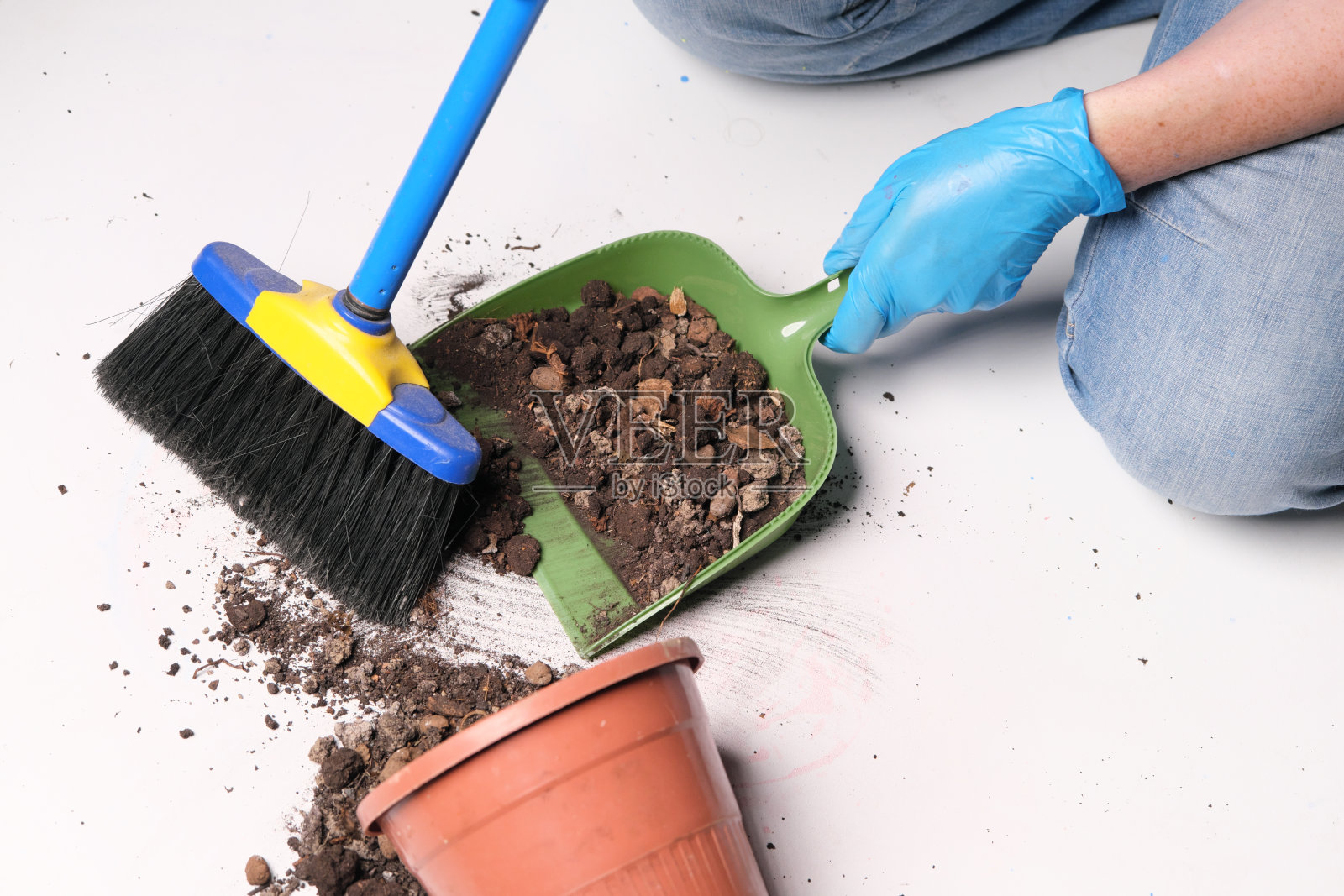 戴着橡胶手套的人手正在清扫散落在白色地板上的花盆照片摄影图片