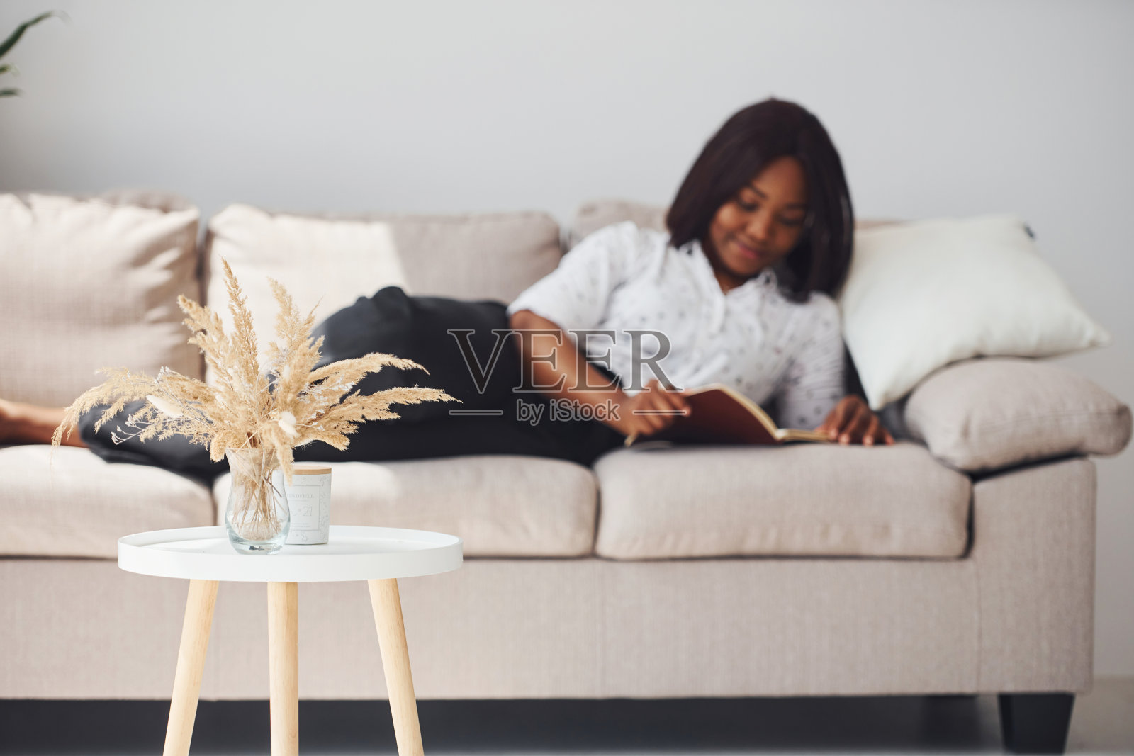 积极的非洲裔美国妇女在白衬衫躺在沙发上,手里拿着记事本照片摄影图片