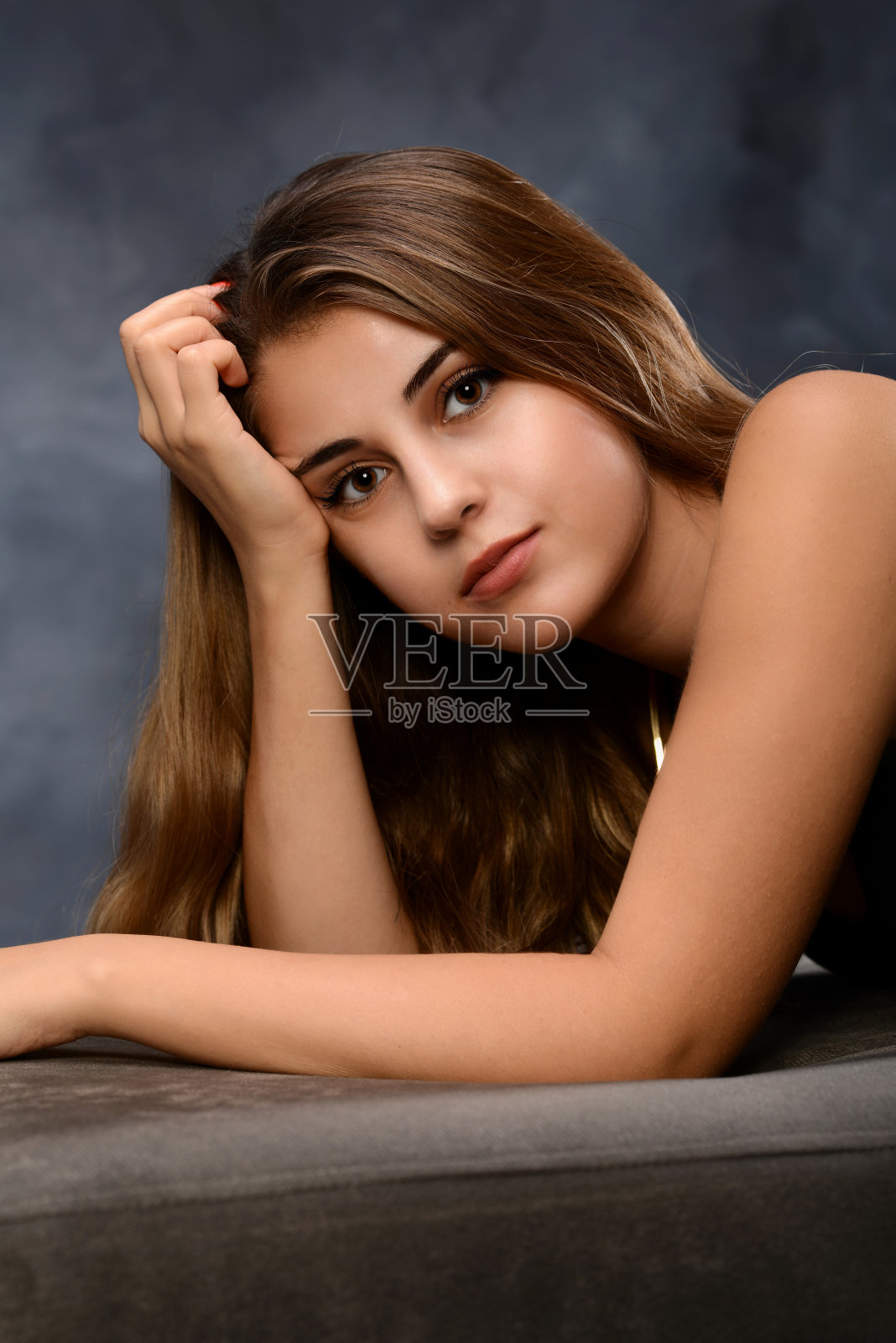 可爱的年轻女子躺在沙发上的工作室与黑色的背景。照片摄影图片