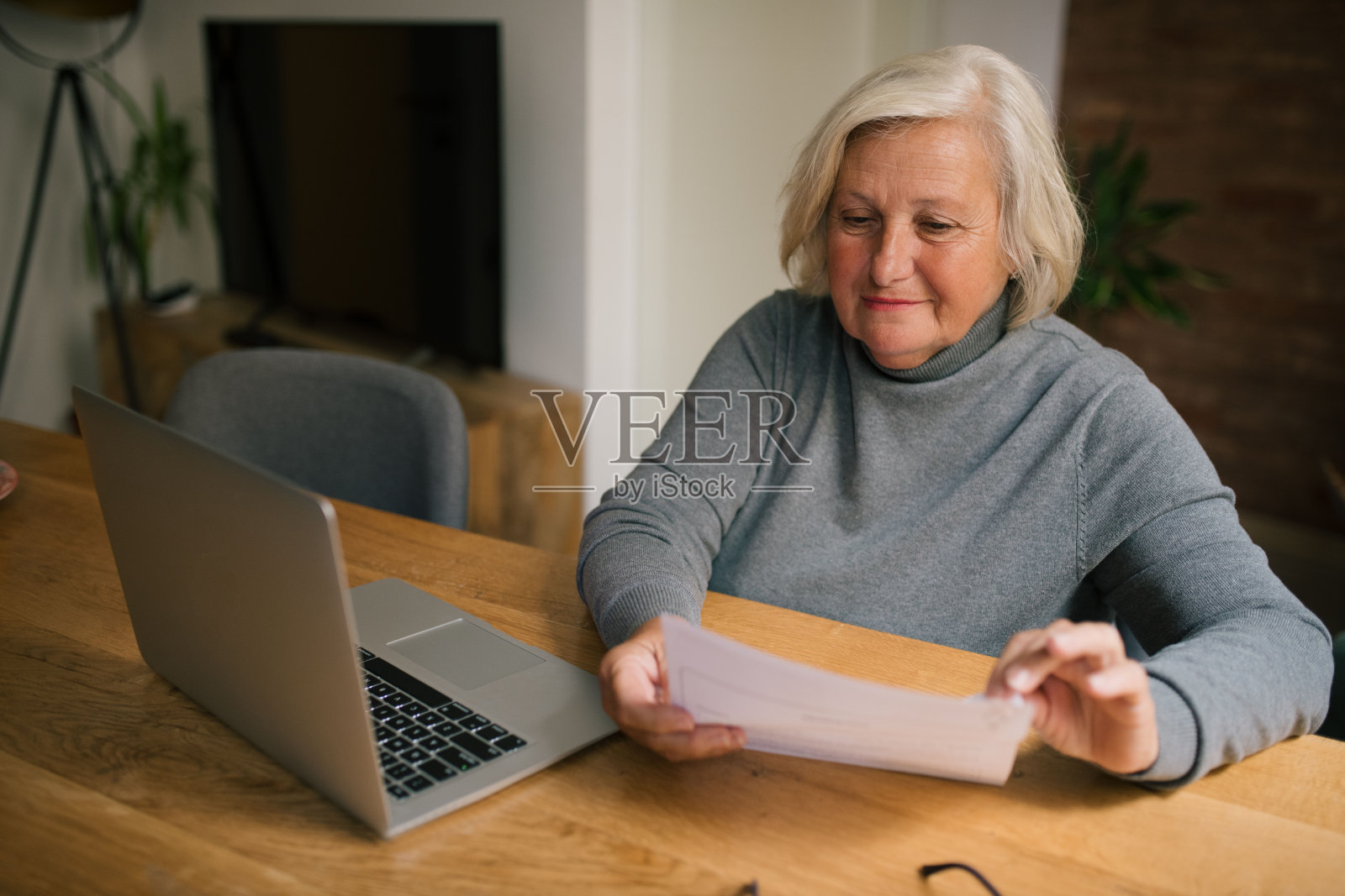 一个金发的老妇人坐在桌旁,手里拿着一些文件。照片摄影图片