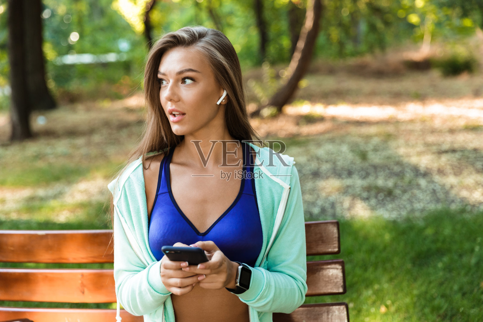 运动女性在公园户外用耳机听音乐用手机。照片摄影图片