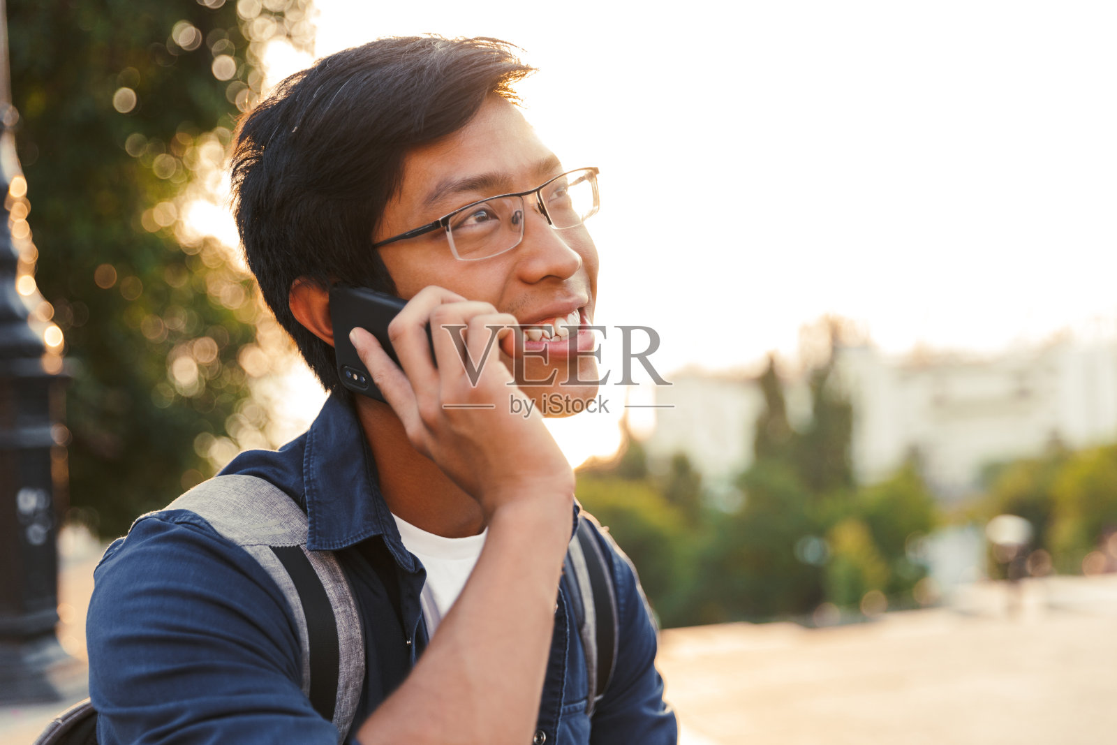 高兴的亚洲男学生在眼镜说话的智能手机照片摄影图片
