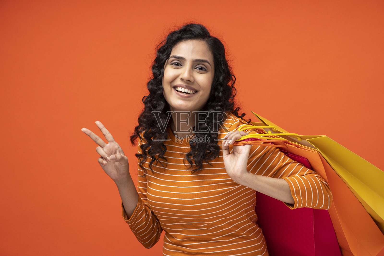 一个背着购物袋的年轻女子孤立地站在橙色的背景下照片摄影图片