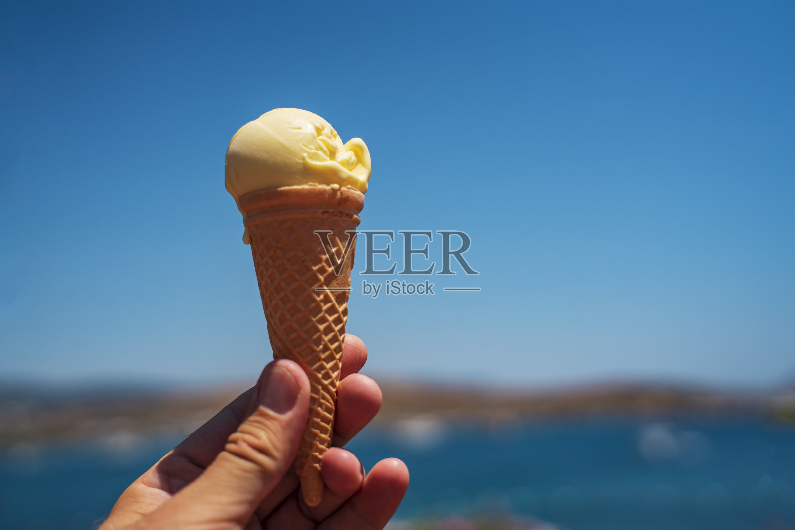 在大海和蔚蓝无云的天空的背景下,华夫饼杯里的冰淇淋。夏季背景,拷贝空间。暑假的概念照片摄影图片