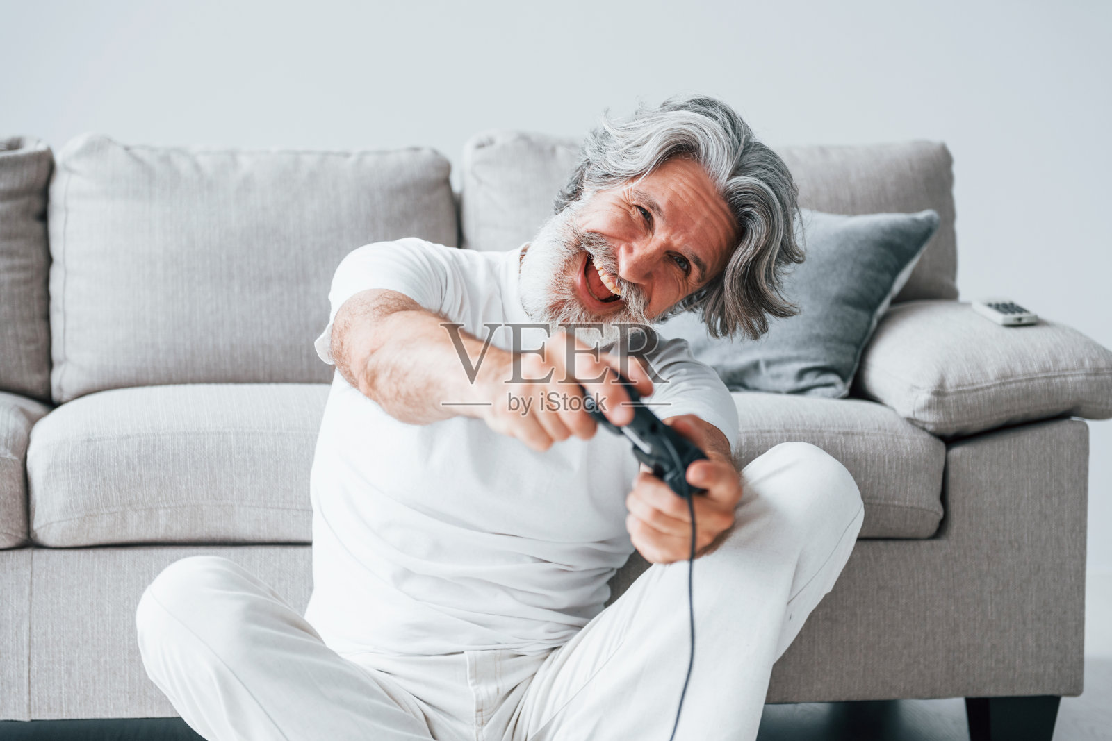 使用控制器玩电子游戏。室内有灰色头发和胡子的高级时尚现代男士照片摄影图片