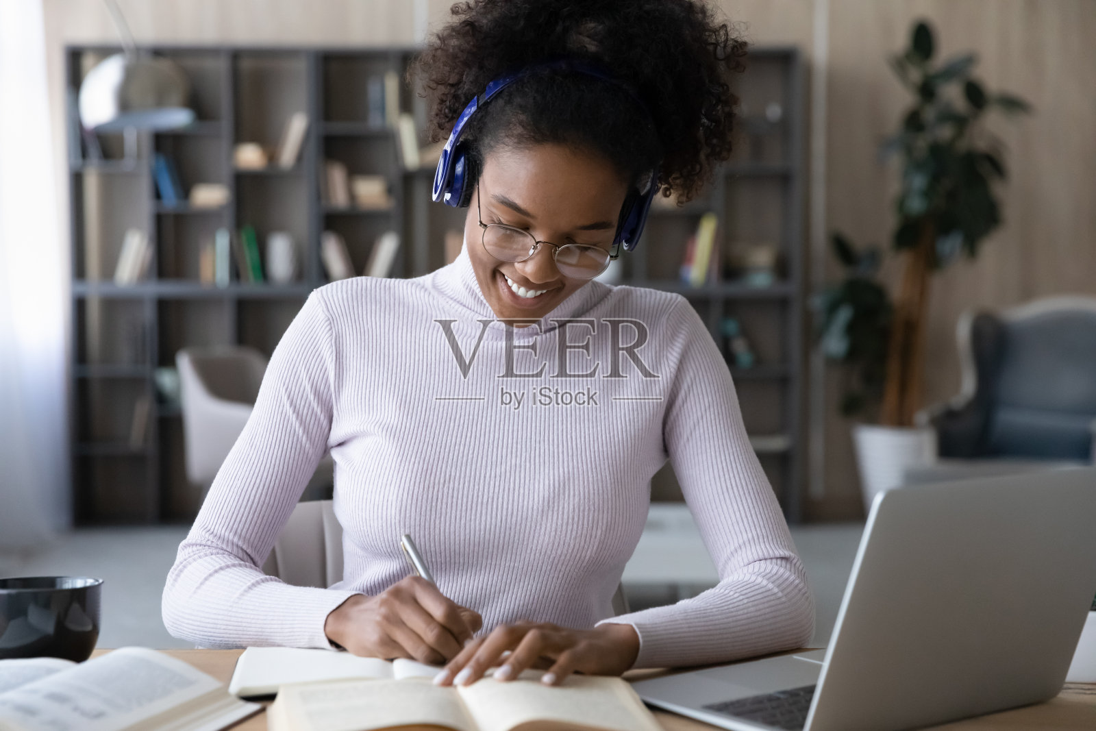 一位带着耳机的微笑的非裔美国女性用笔记本电脑做笔记照片摄影图片