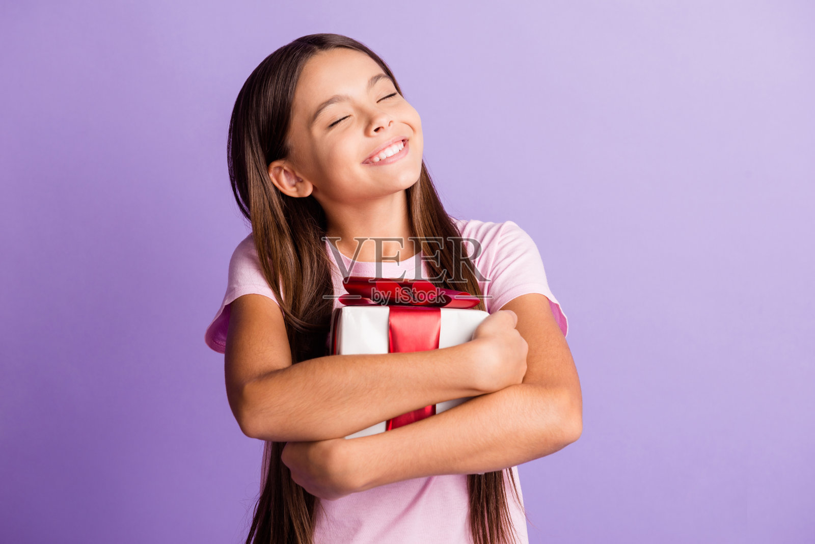照片中漂亮的女生穿着粉红色的t恤拥抱着礼物盒孤立的紫色背景照片摄影图片