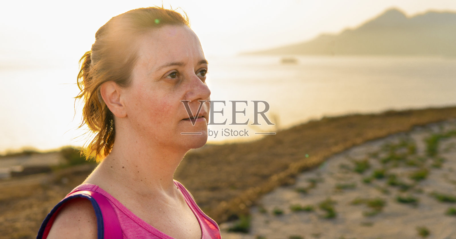 在海边的公园里,一名美丽的白人女子在日落时微笑着,她的脸很可爱。照片摄影图片