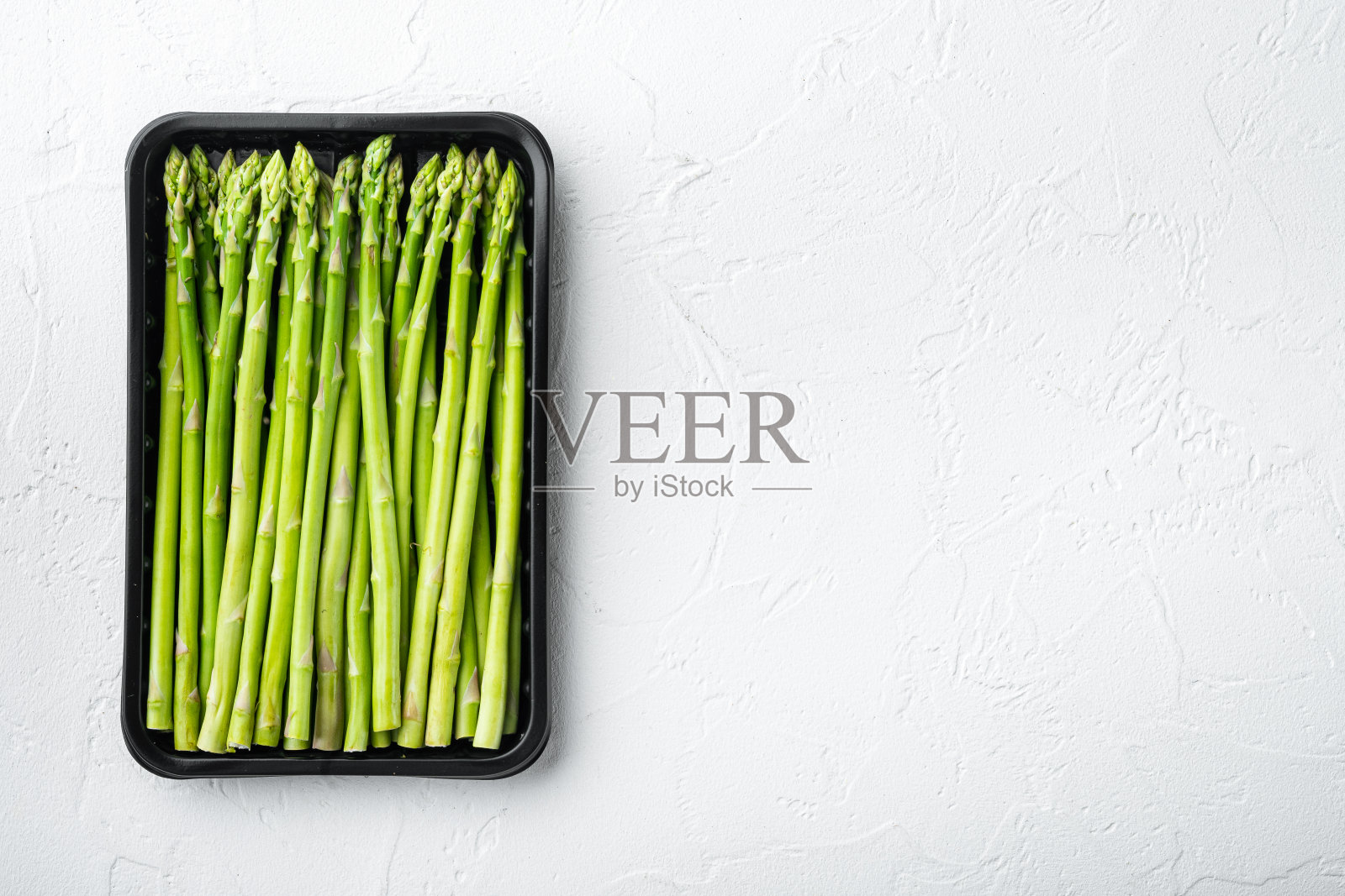 一束新鲜芦笋,在塑料市场容器,在白色的石头背景,顶部视图平铺,文本复制空间照片摄影图片