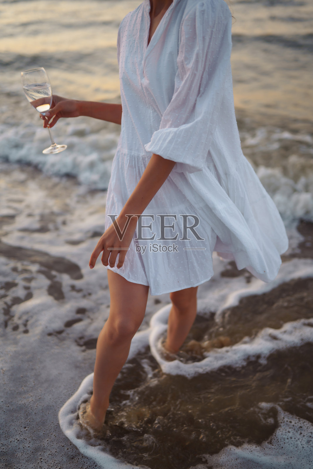 一个年轻快乐的女人,穿着飘逸的白色连衣裙,沿着海岸走着。照片摄影图片