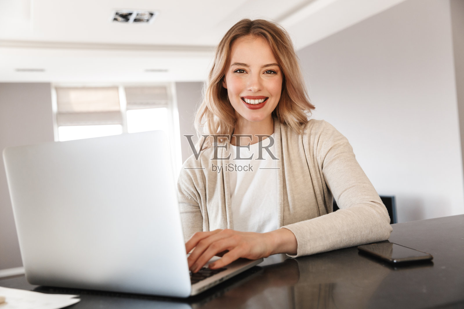 漂亮的金发女人坐在家里用笔记本电脑。照片摄影图片