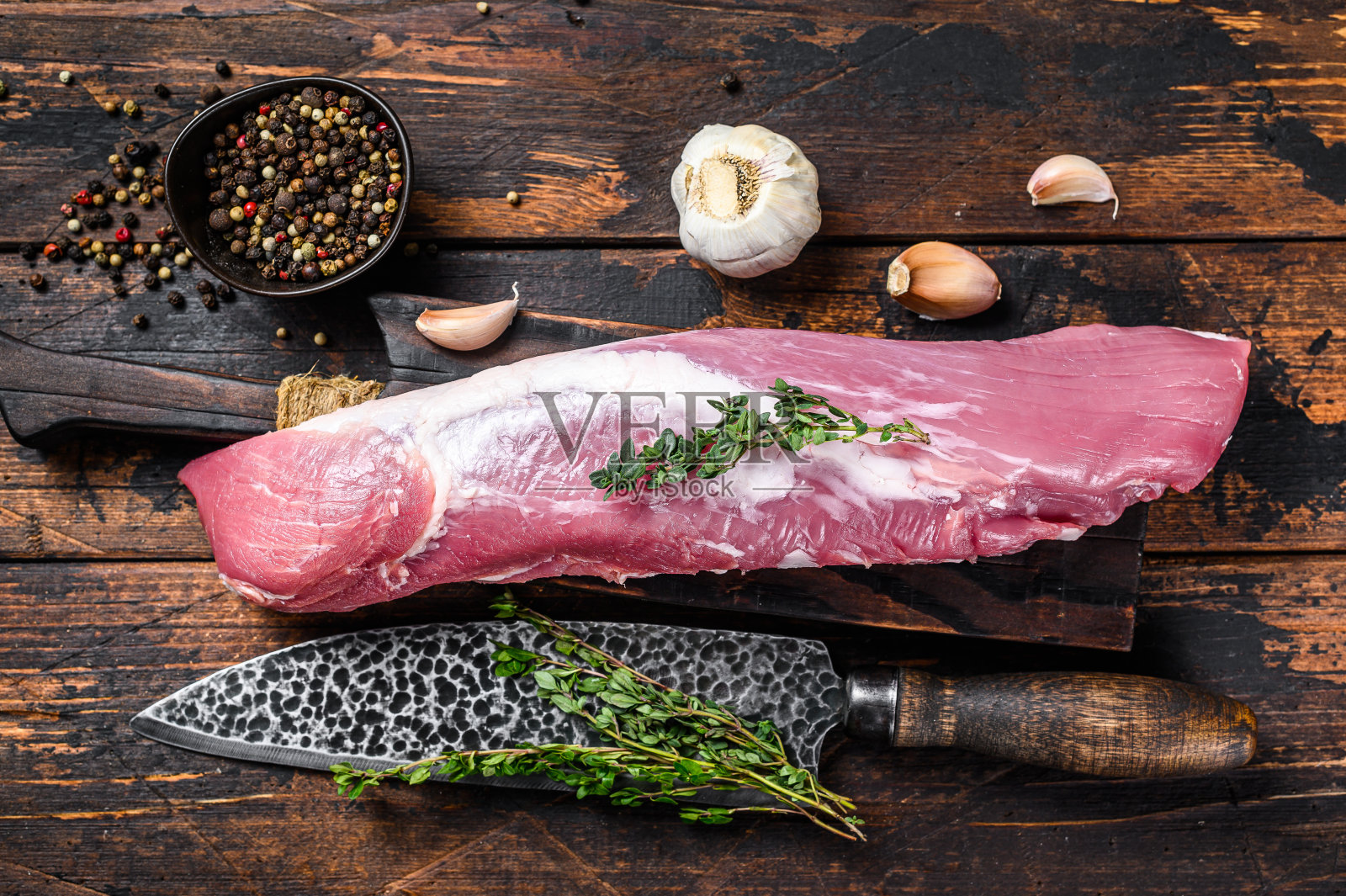 生鲜猪里脊肉放在砧板上,用切肉刀切下。深色木制背景。俯视图照片摄影图片