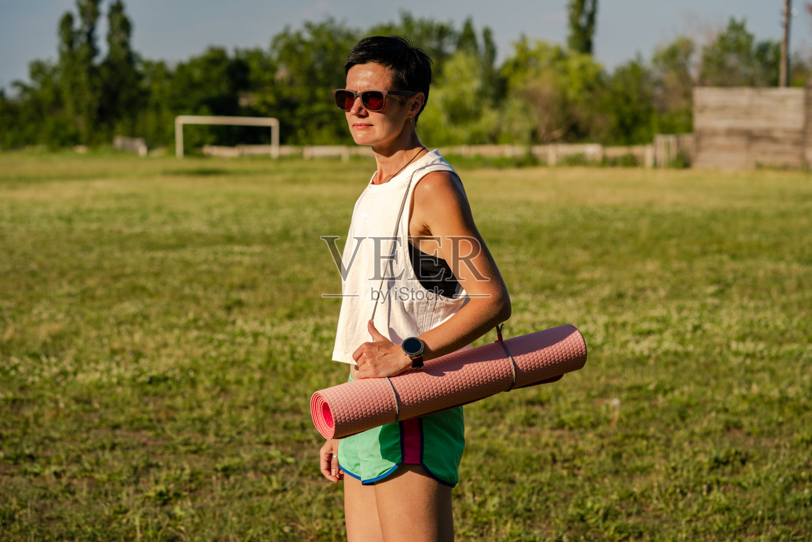 年轻美丽的女人与瑜伽垫在一个公园,短黑发,太阳镜和短裤,户外运动在夏天,苗条的健身女孩运动服,女性在锻炼训练照片摄影图片