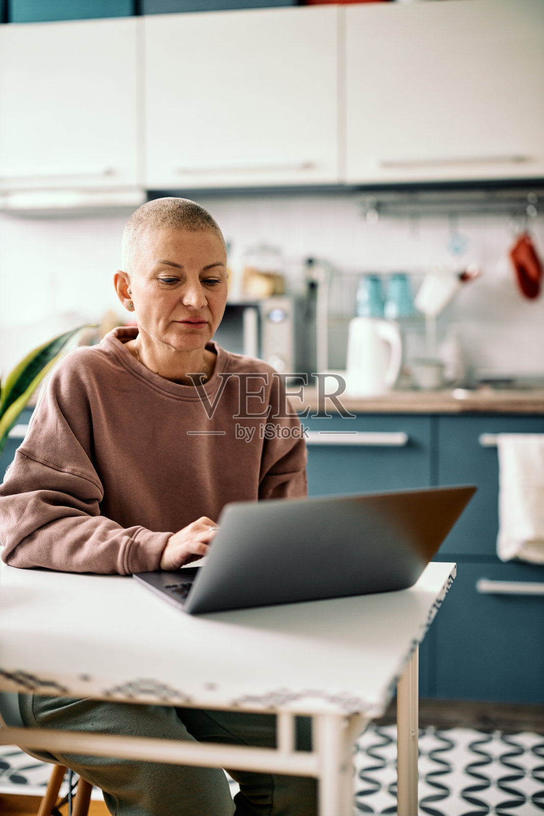 迷人的高级商人女性穿着随意坐在厨房和工作笔记本电脑。照片摄影图片
