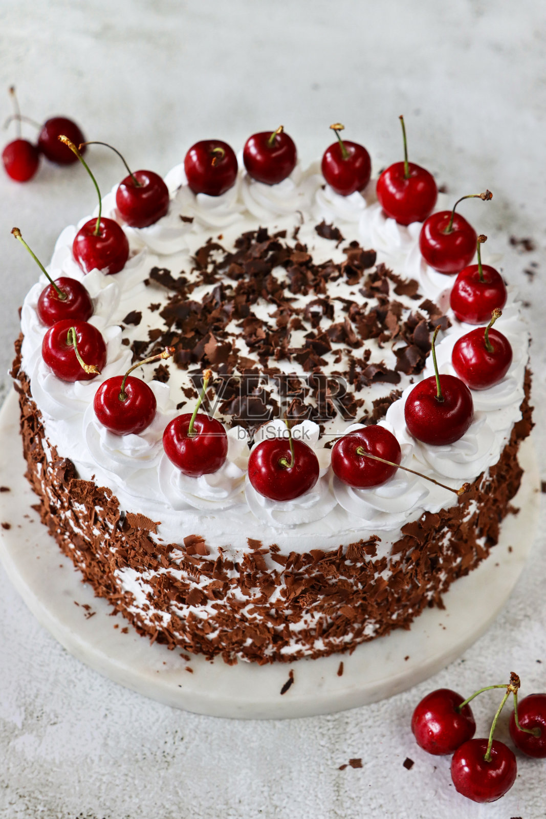 蛋糕架上的黑森林蛋糕图片,上面有玫瑰形的奶油蛋糕,上面有樱桃,奢华的巧克力蛋糕上覆盖着奶油和巧克力屑,大理石效果的背景,高架的视野照片摄影图片