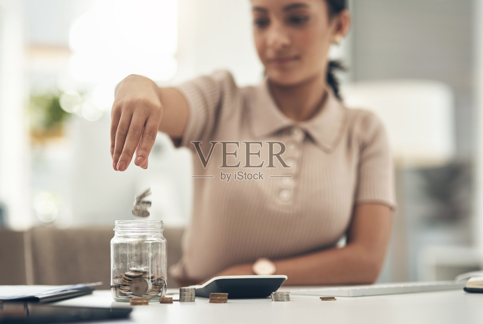 在一间办公室里,一个完全认不出来的女商人正在往玻璃瓶里装硬币照片摄影图片