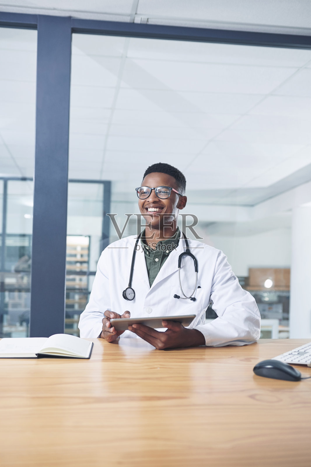 一个英俊的年轻医生独自坐在诊所的办公室里使用他的电子平板电脑照片摄影图片