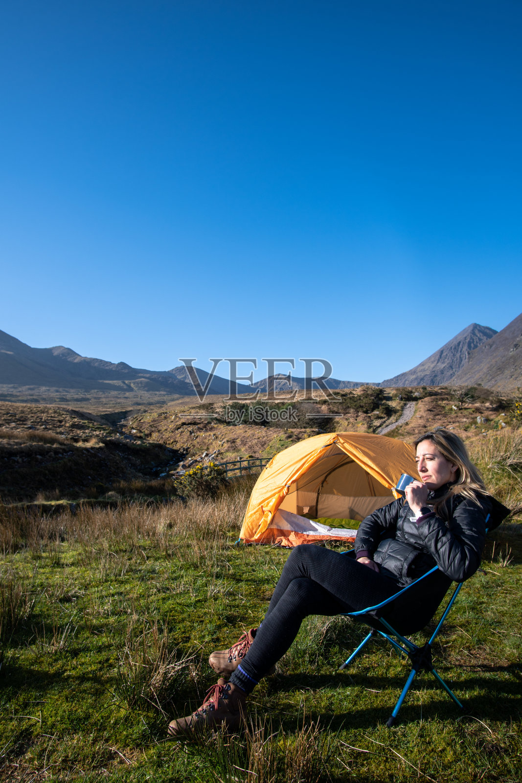 年轻女子坐在营地里欣赏着山景,喝着咖啡照片摄影图片