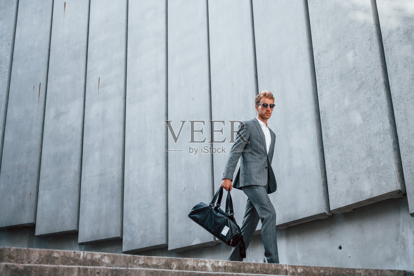 从楼梯下去。身着灰色正装的年轻商人在城市的户外照片摄影图片