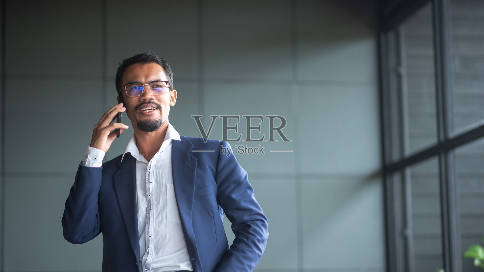 年轻英俊的商人戴着眼镜,坐在办公室的沙发上用触控板工作。照片摄影图片