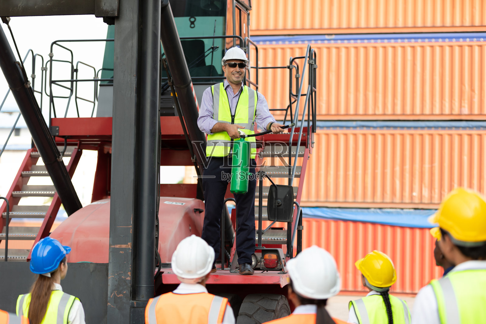 男工程师站在起重机上使用灭火器与工厂工人在集装箱仓库储存照片摄影图片