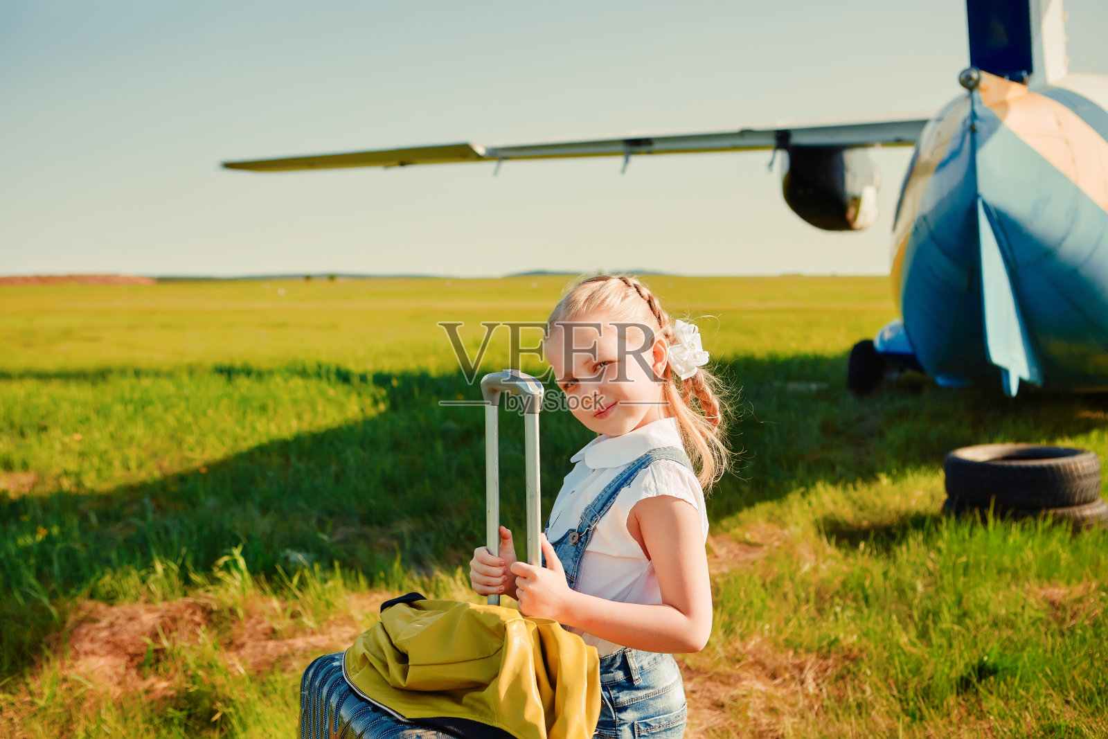 停机坪上一个小女孩提着一个手提箱准备坐飞机旅行。照片摄影图片