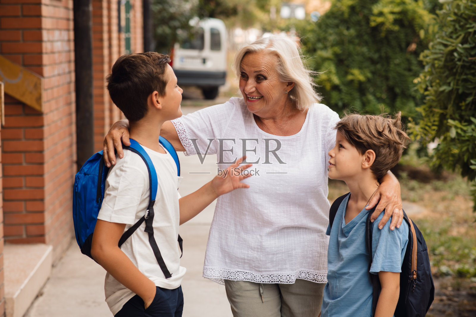一位金发的老妇人在学校门口和她的孙子孙女们说话。照片摄影图片