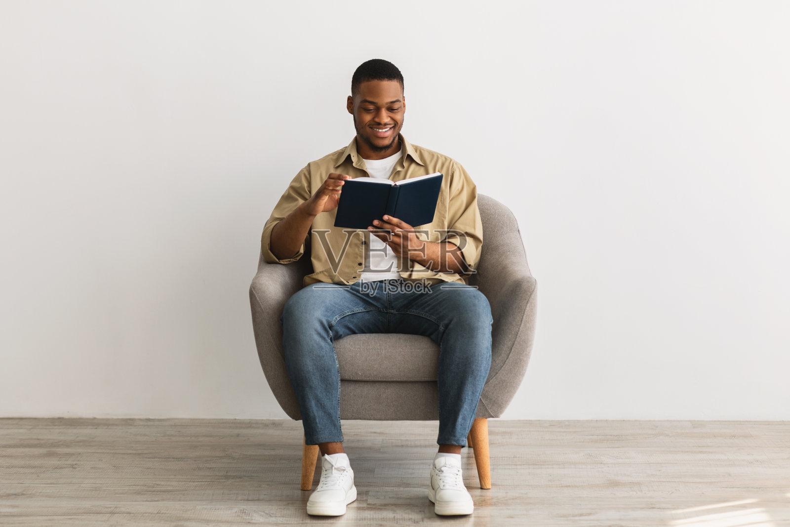 一个黑人坐在扶手椅上看书,背景是灰色的照片摄影图片