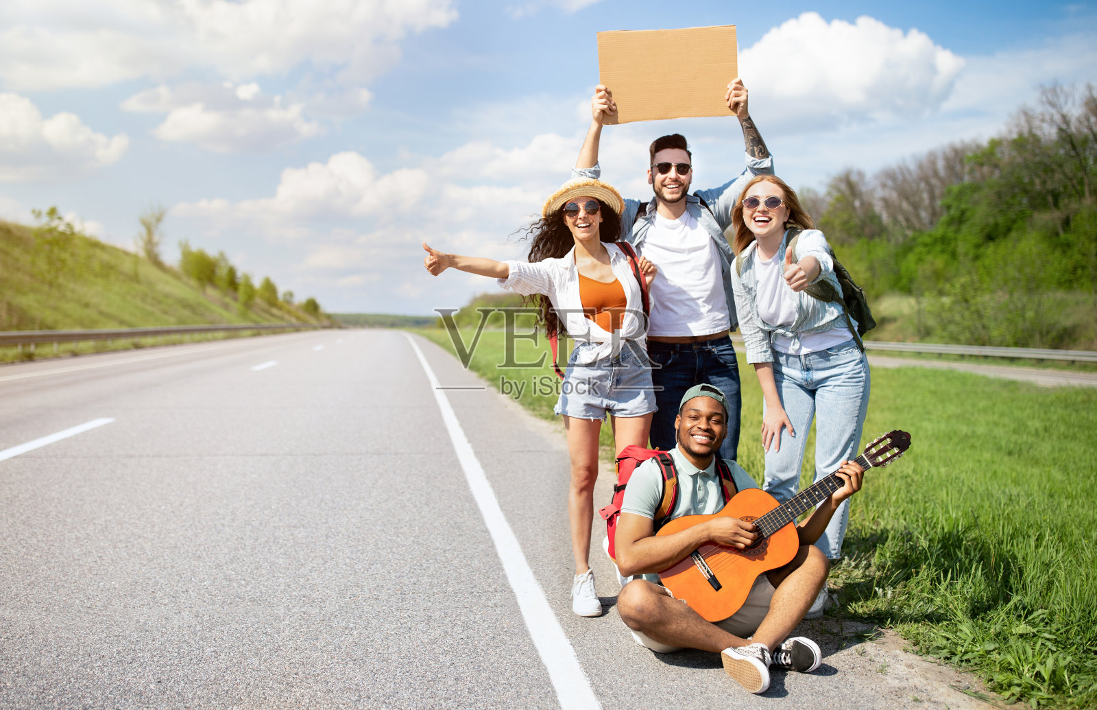 各式各样的朋友们,背着背包,弹着吉他,在高速公路上搭便车,搭顺风车,进行夏日冒险照片摄影图片
