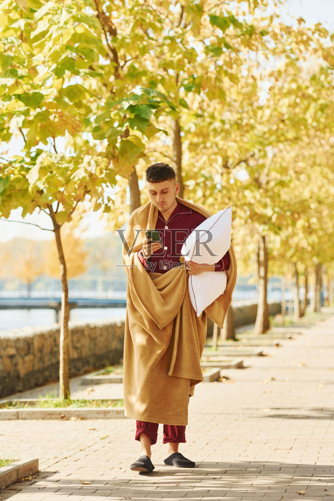 拥有智能手机。一个穿着睡衣的年轻人走在大街上。感觉困了照片摄影图片