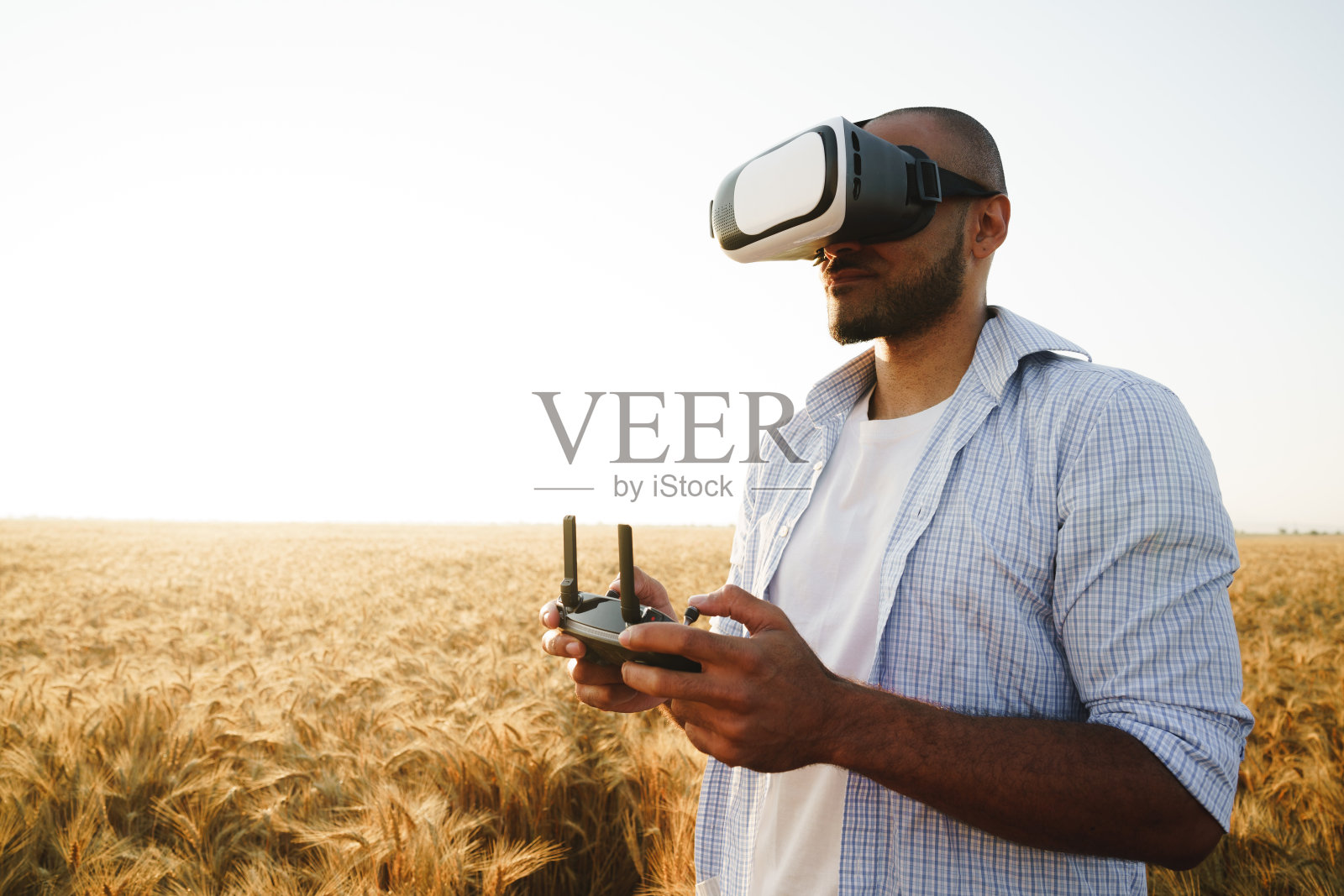 一个年轻人戴着虚拟现实眼镜站在麦田里看日落照片摄影图片