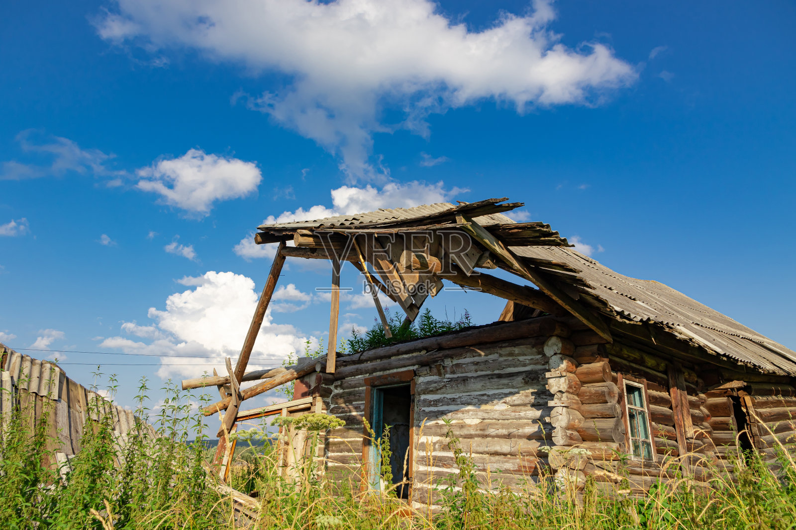 一个晴朗的夏日,破旧的木屋被遗弃在蓝天白云的映衬下。特写镜头照片摄影图片