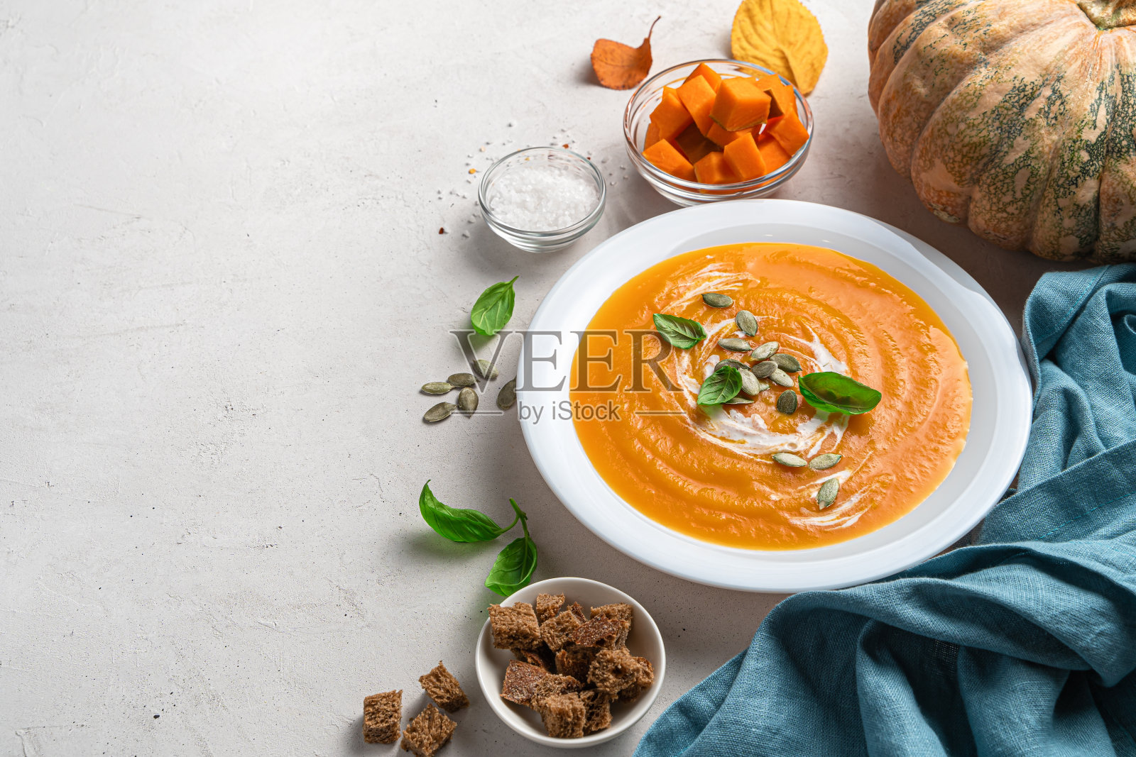 南瓜奶油汤,灰色背景上有南瓜籽和罗勒。侧视图照片摄影图片