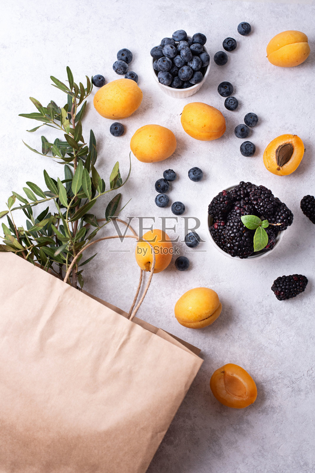 熟透的杏子,蓝莓,黑莓散落在白色的背景上,夏天买浆果,纸袋和杏子,蓝莓。照片摄影图片