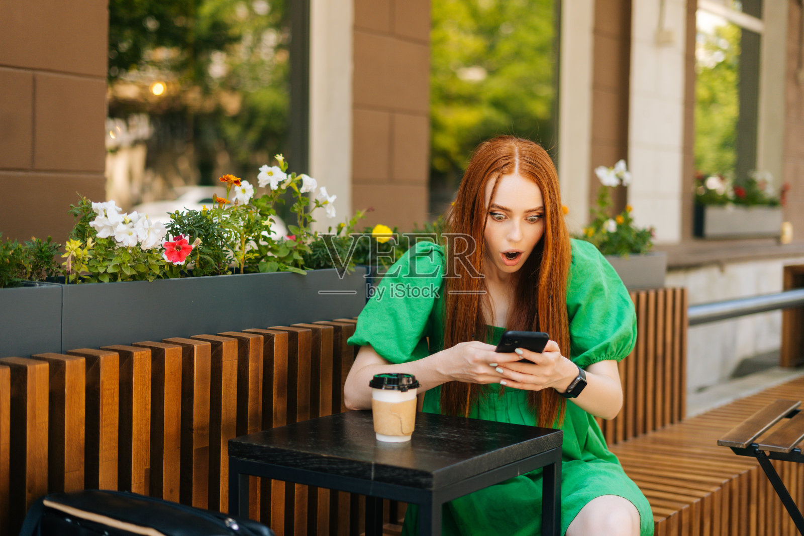 兴奋快乐的年轻女子看着手机屏幕庆祝在线获胜,坐在桌子上的咖啡杯在户外咖啡馆露台。照片摄影图片