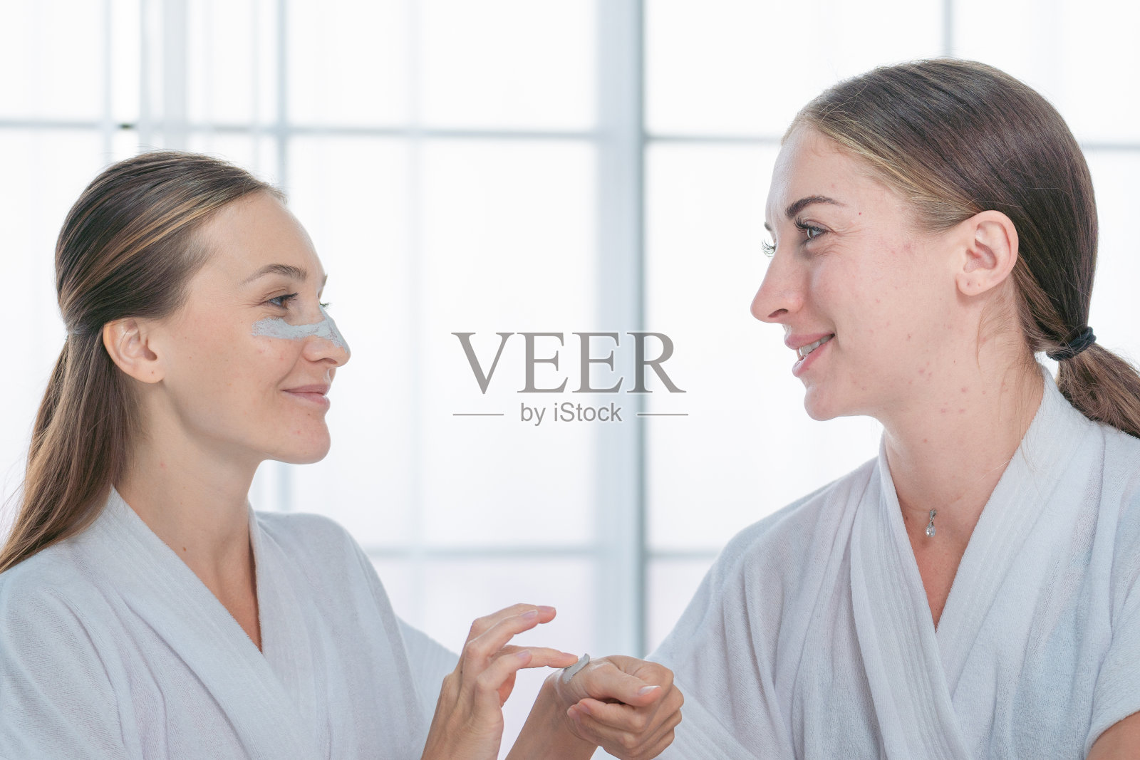 自然人像两位女性脸上用微笑的年轻女性泡沫霜在脸颊上洗脸。皮肤护理及卫生程序处理。特写画室人像在白色复制空间的墙壁上。照片摄影图片