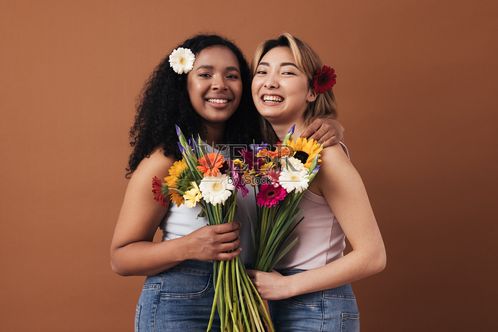 两个不同种族的年轻女子,头发上插着花束和鲜花,在棕色背景下摆姿势照片摄影图片