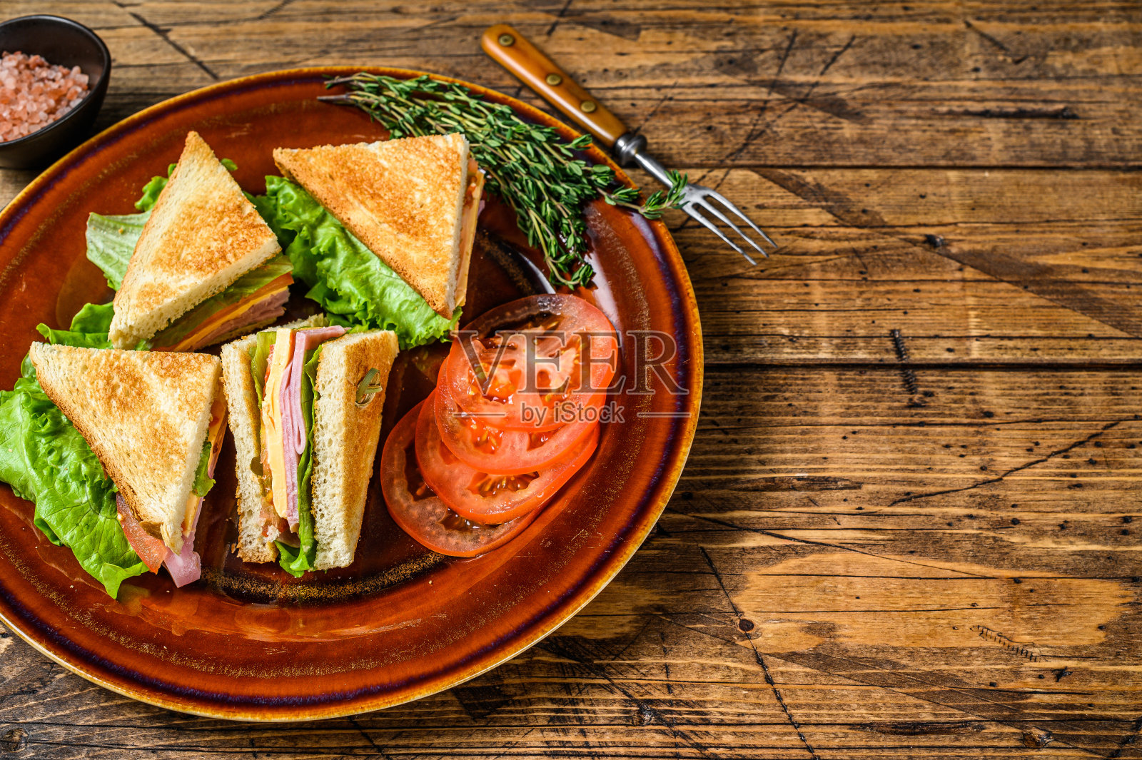 烤俱乐部三明治与猪肉火腿,奶酪,西红柿和生菜在盘子。木制背景。前视图。本空间照片摄影图片