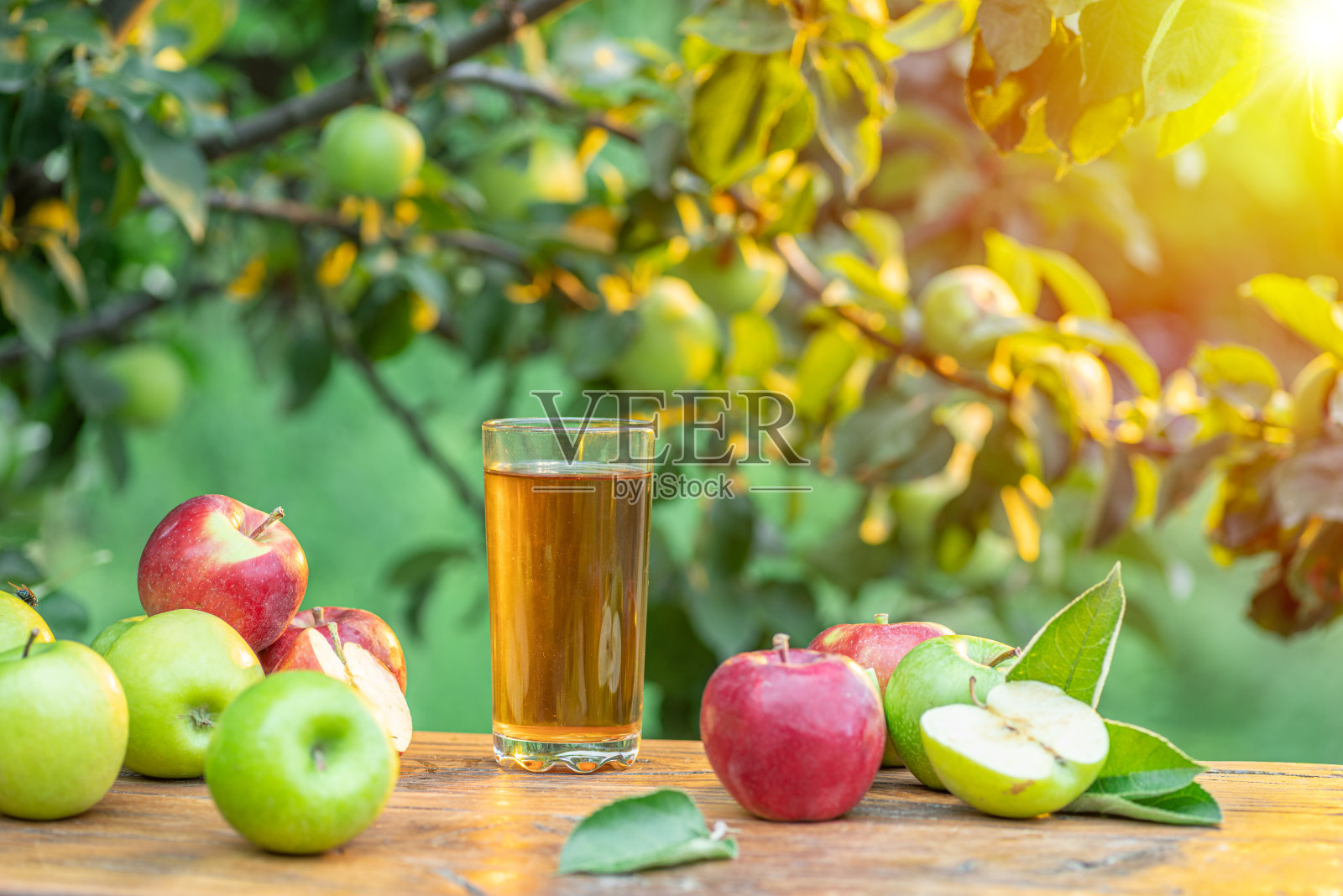 新鲜苹果汁和有机苹果放在木桌上。夏天的果园在傍晚阳光的映衬下。照片摄影图片