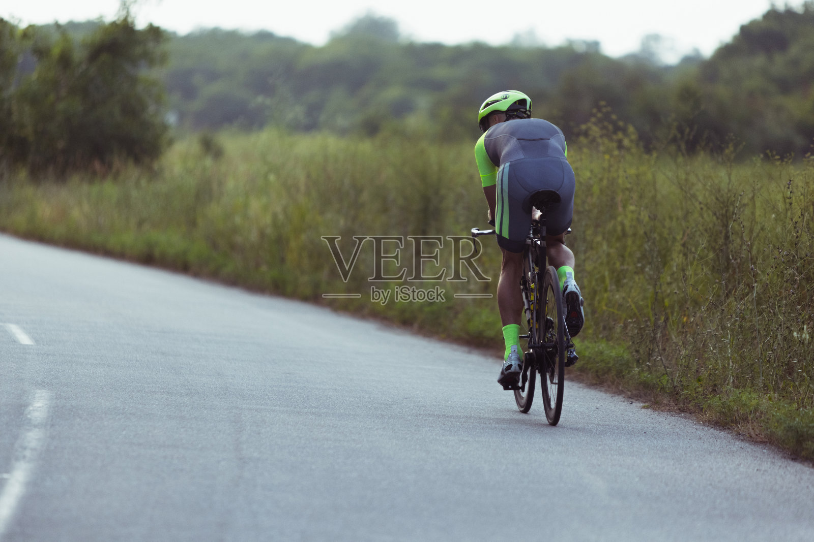 年轻的男子铁人三项运动员在开阔的道路上骑自行车。职业运动员在晴朗的夏日从事铁人三项运动照片摄影图片
