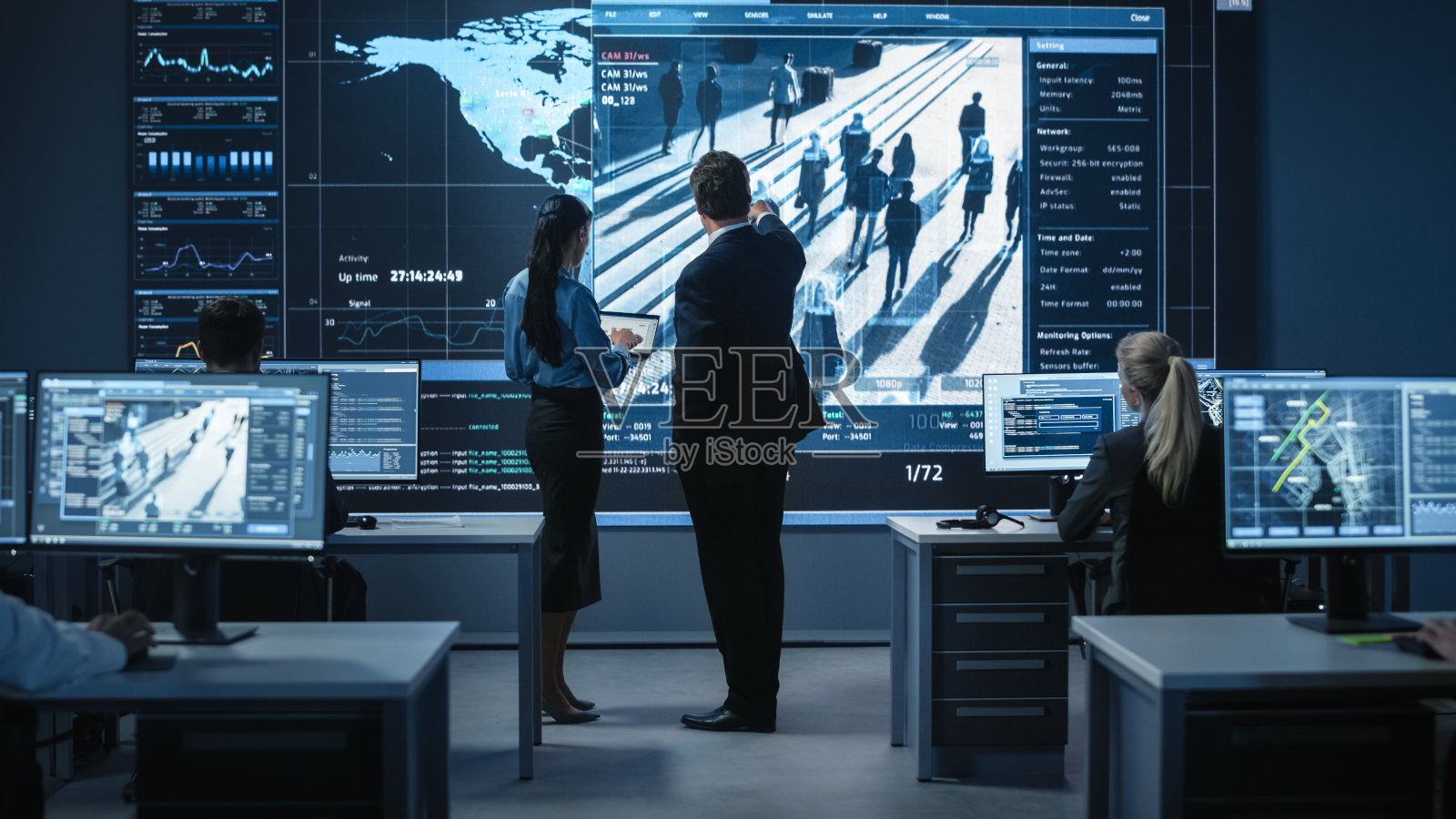 中年男女公务员站在装有卫星监控录像和人脸识别软件的大数码屏幕旁讨论工作事宜。警察调查人员在工作。照片摄影图片