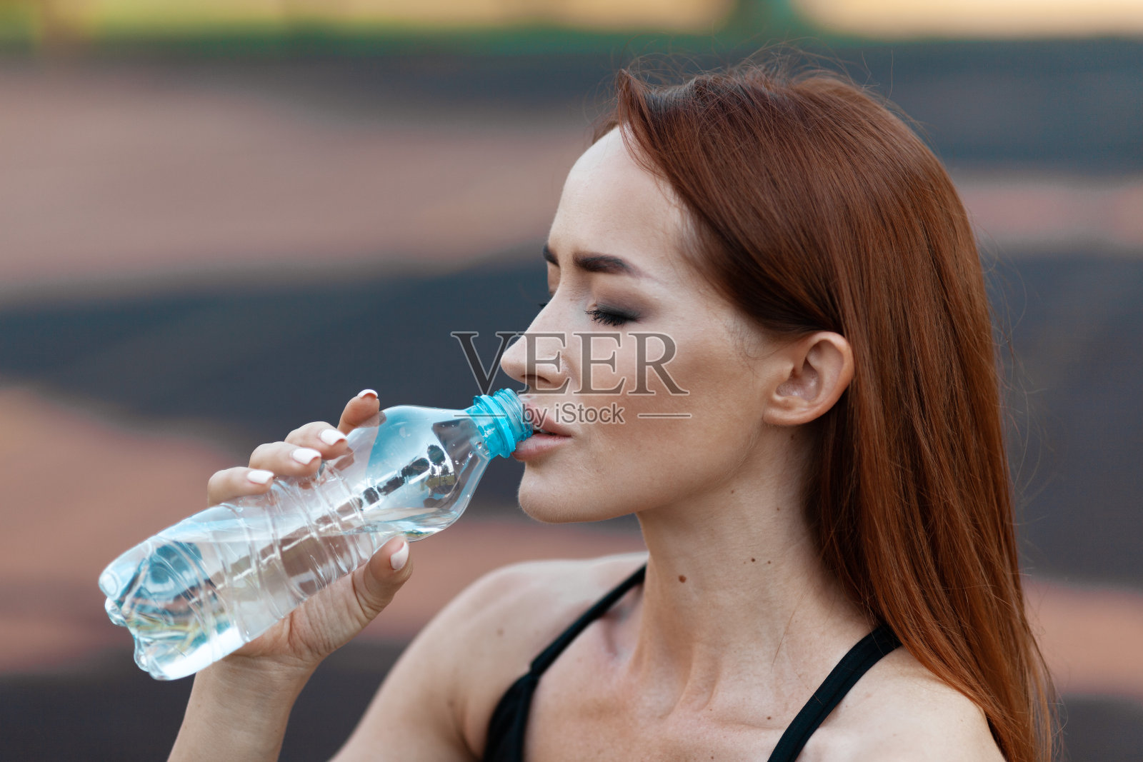 一个成年妇女在锻炼后喝瓶装水。一个强壮的女运动员的肖像照片摄影图片