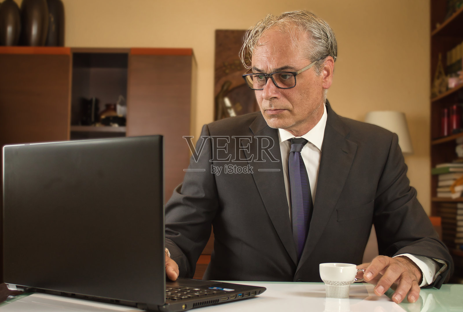 商人喝着咖啡,在家里用笔记本电脑远程办公照片摄影图片