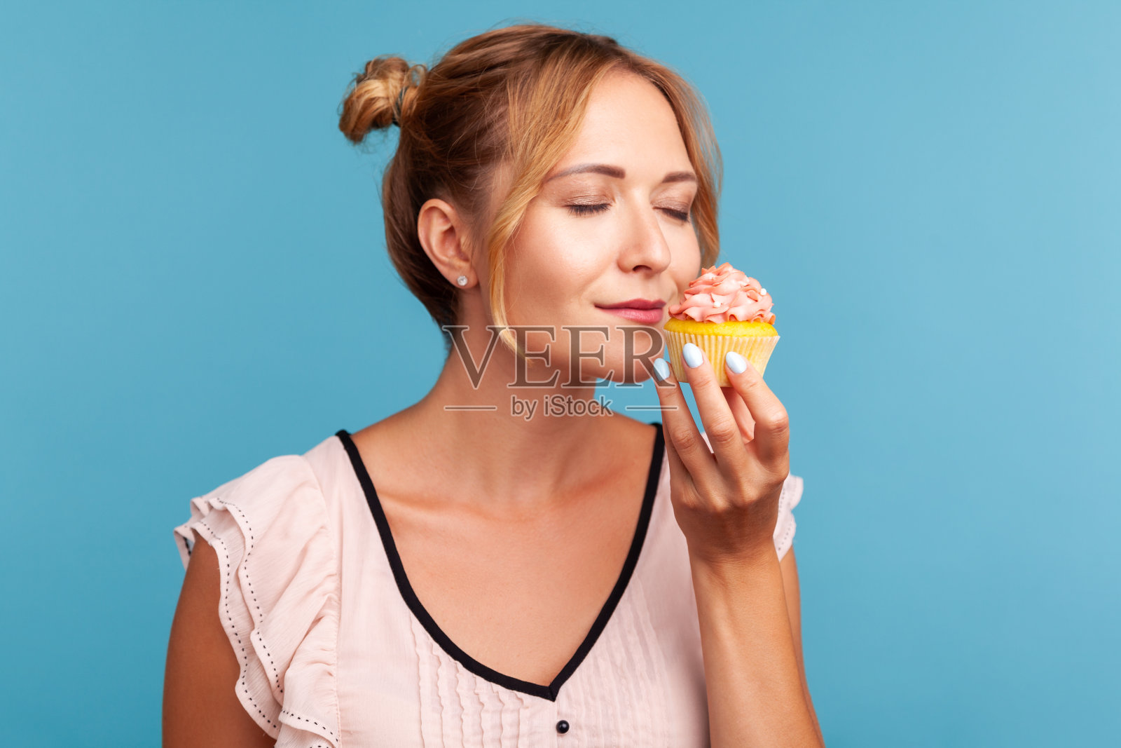 美丽的金发女郎的肖像,手里拿着发髻,闭着眼睛享受着美味的气味,渴望着吃甜点。照片摄影图片