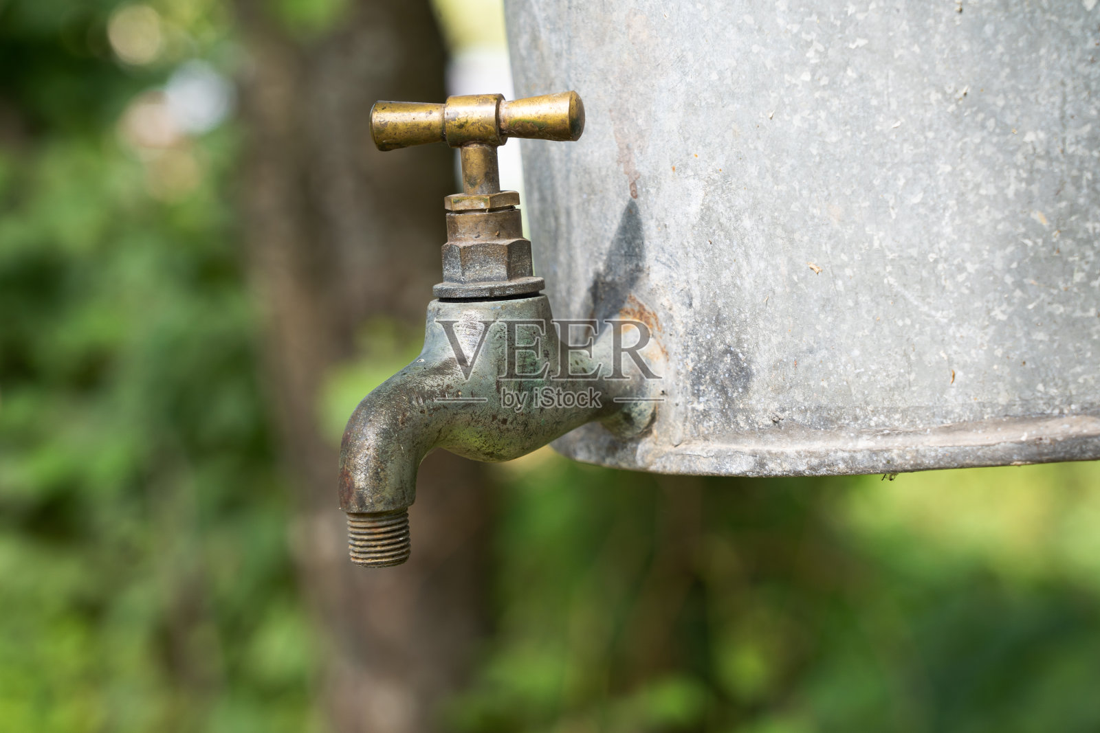 一个老式的水龙头连接在镀锌的花园水槽上。它有一个老化的灰色金属表面和一个黄黄铜把手。背景。纹理。照片摄影图片