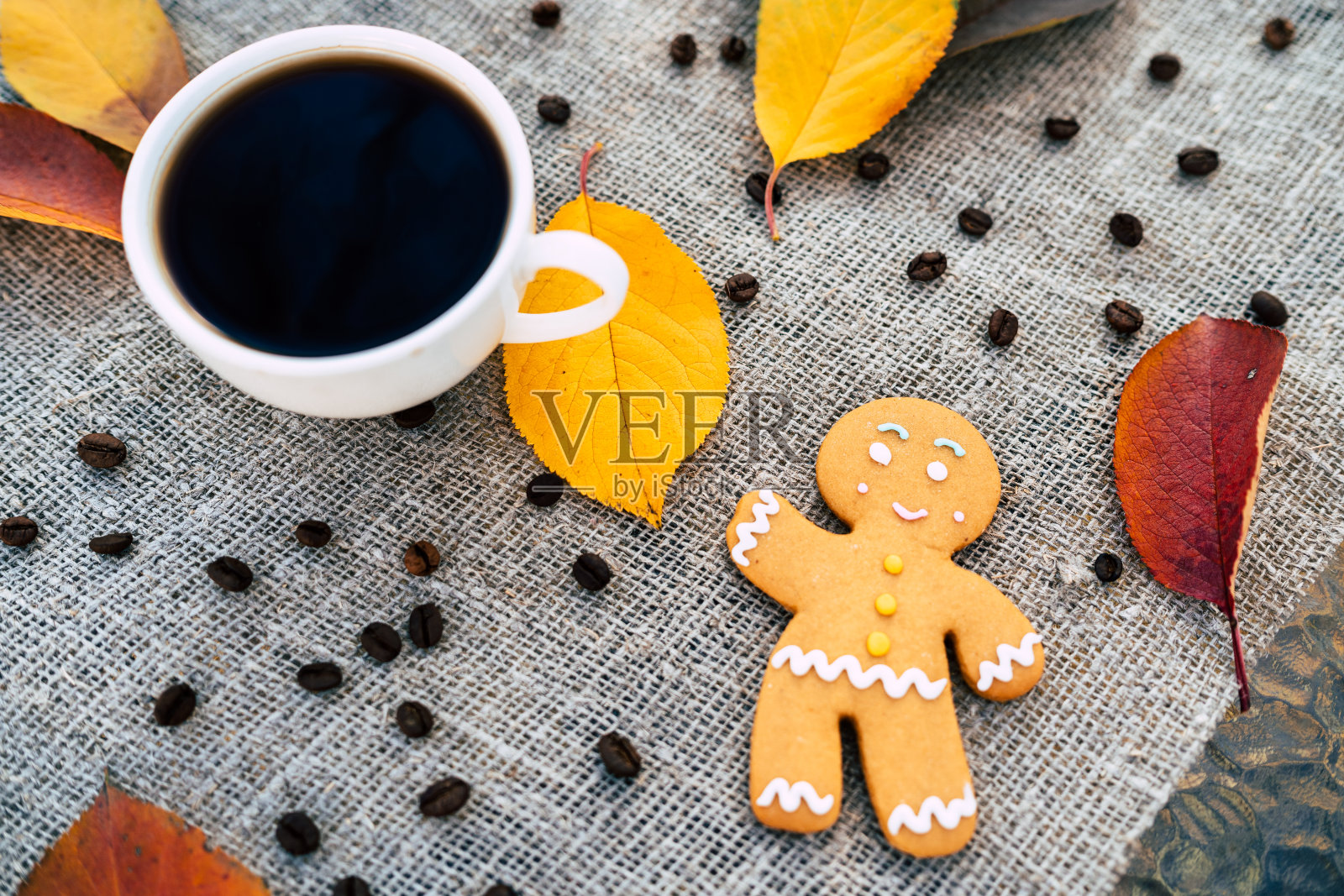 姜饼人和秋叶旁的咖啡。顶视图的甜姜饼人和一杯浓咖啡放置在五彩缤纷的秋叶附近的亚麻布照片摄影图片